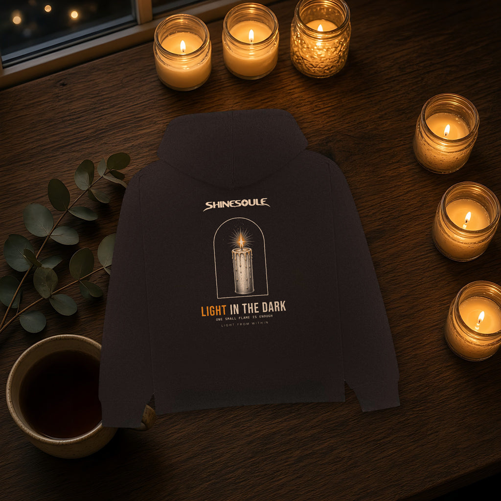 Black Light In The Dark Graphic Hoodie on a dark wooden table surrounded by lit candles, eucalyptus and a cup of coffee