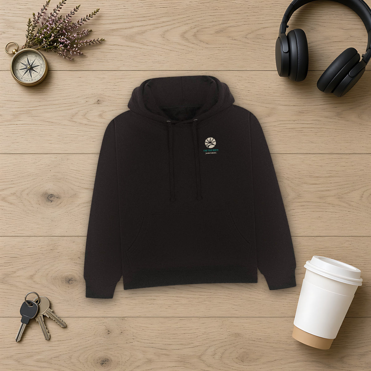 Black Northern Light Graphic Hoodie flat lay on light oak with headphones, keys and a takeaway coffee