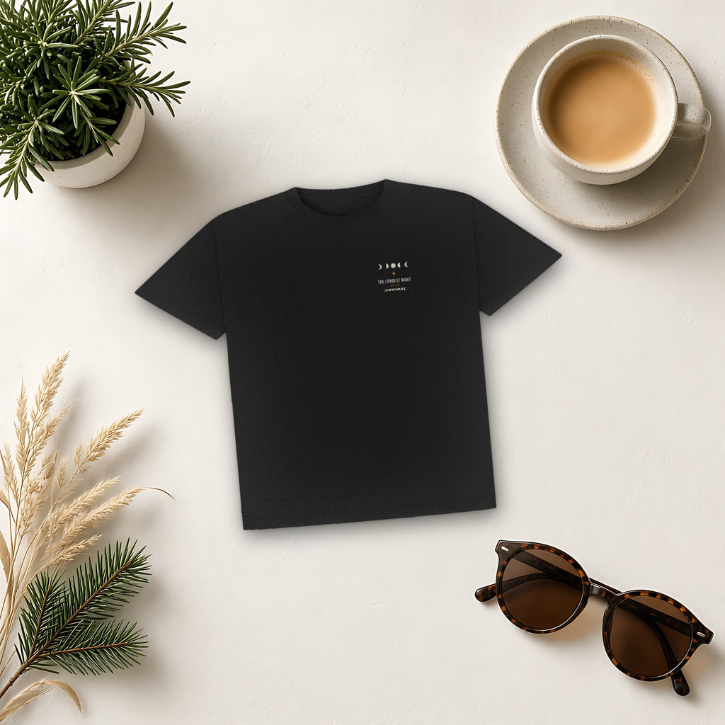 Black Solstice Graphic T-Shirt flat lay on cream with sunglasses, dried grasses, a plant and a coffee