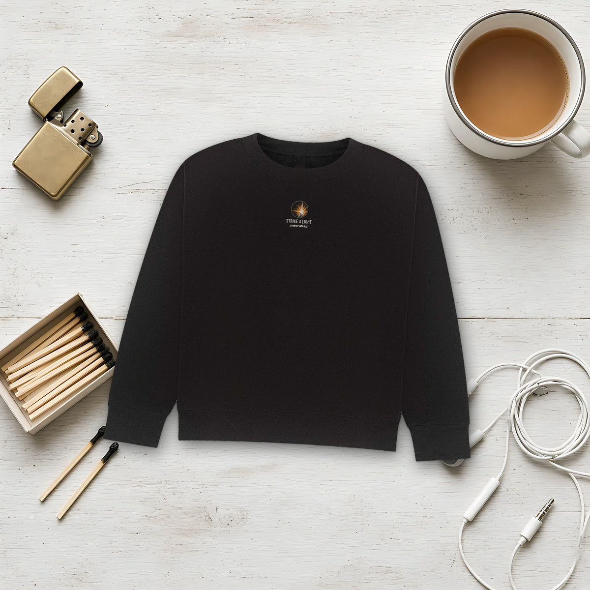 Black Strike A Light Graphic Crewneck Sweatshirt flat lay on white with a lighter, a box of matches, earphones and a coffee